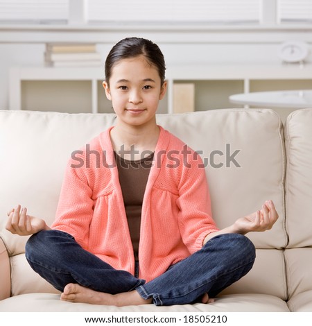 Relaxed girl sitting cross-legged meditating on sofa in livingroom