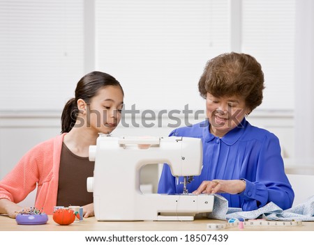 Curious granddaughter watching creative grandmother use sewing machine to make clothing