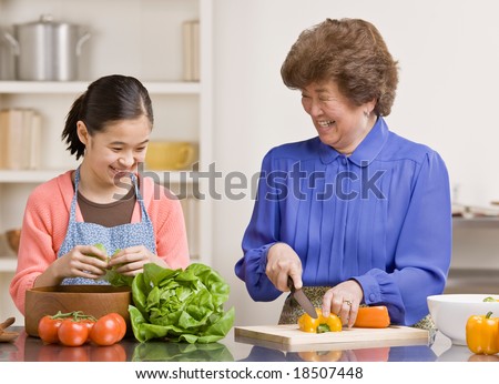 Helpful granddaughter preparing wholesome salad with grandmother in kitchen for dinner
