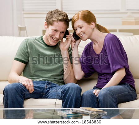 Couple sitting on sofa and sharing headphones to listen to music