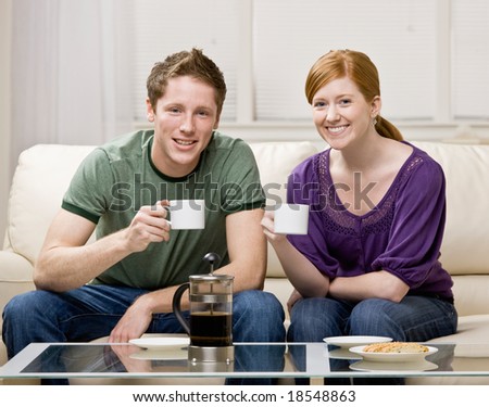 Happy couple sitting on sofa in livingroom drinking fresh coffee