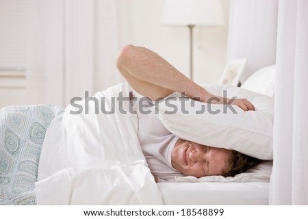 Annoyed man using pillow to block out noise while trying to sleep