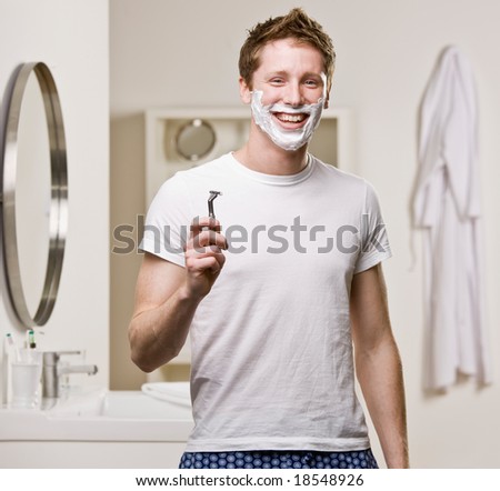 Man in pajamas in bathroom using shaving foam and shaving his face with razor