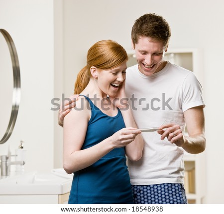 Excited, happy couple in bathroom viewing positive pregnancy test