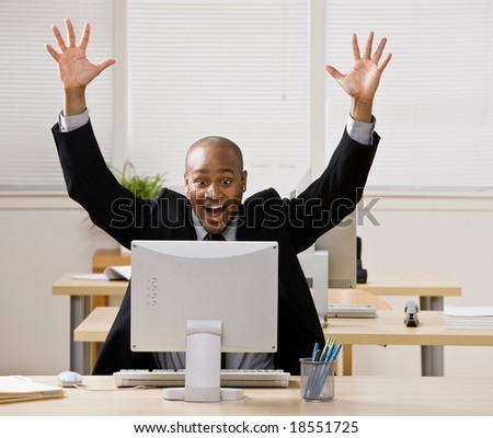 Excited businessman sitting at desk cheering and celebrating his success