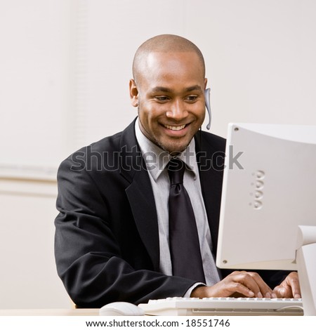 Confident businessman talking on headset while typing on computer at desk