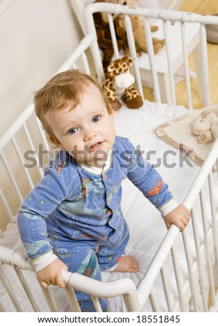 Determined toddler boy trying to climb out of crib in bedroom