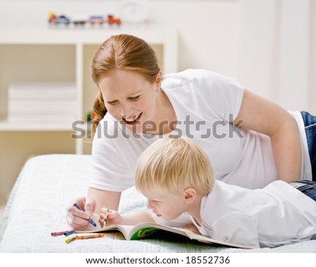 Devoted mother coloring in coloring book with son on bed in bedroom
