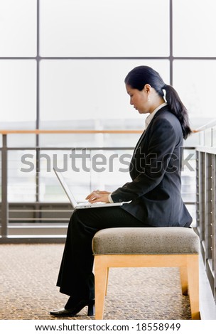 Side view of Asian businesswoman working on laptop in office lobby