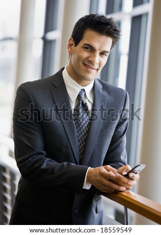 Confident businessman text messaging on cell phone in office lobby