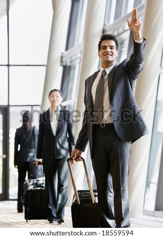 Business traveler pulling suitcase and gesturing to co-worker