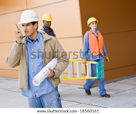 Busy construction workers carrying ladder, blueprints and talking on cell phone