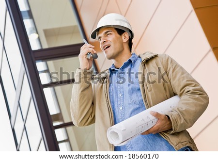Low angle view of construction worker talking on cell phone and holding blueprints