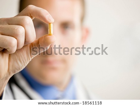 Close up of doctor holding small yellow pill