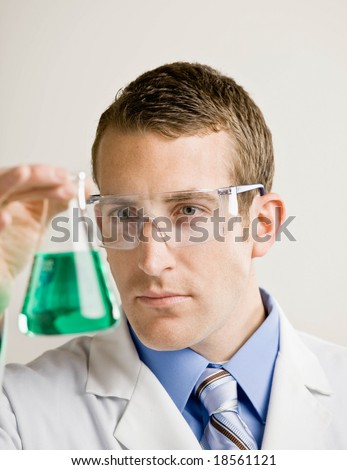 Research scientist wearing safety goggles examining beaker of liquid in laboratory