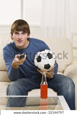 Cute teenager with remote and soccer ball facing the camera, with drink on the table. vertical.