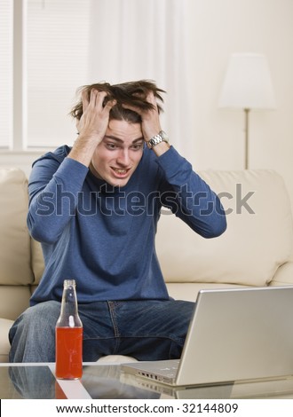 Cute guy pulling his hair out while looking at the computer drinking an orange soda. vertical