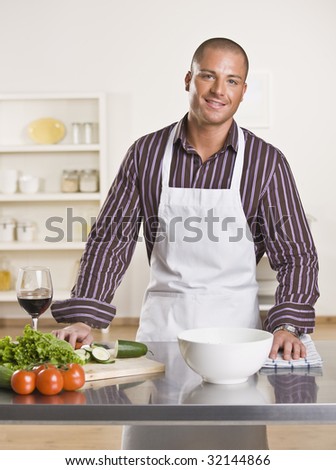 Attractive male chef in the kitchen with vegetables and a glass of wine on the counter. Vertical