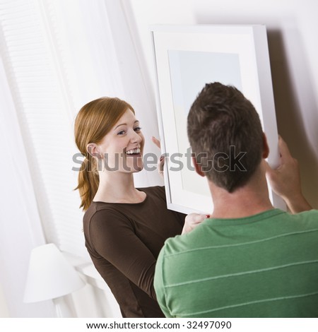 An attractive young couple hanging a picture frame in their home. Square composition.