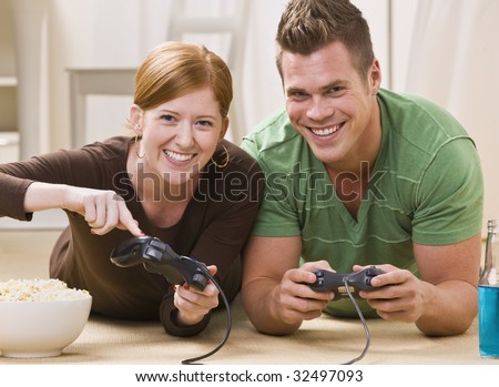 A happy young couple smiling and playing video games together in their home. Horizontally framed shot.