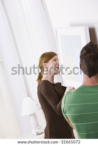 A young couple hanging a picture frame together in their home.  Vertically framed shot.