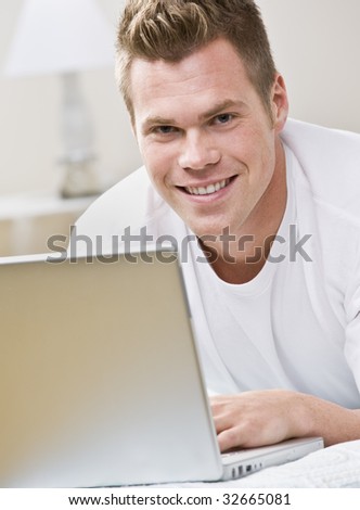 An attractive young man smiling and using a laptop.  Vertically framed shot.