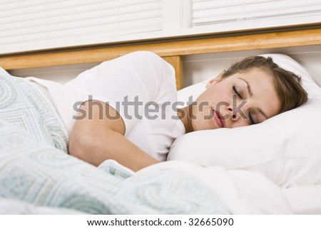 A beautiful young woman is sleeping in her bed.  Horizontally framed shot.