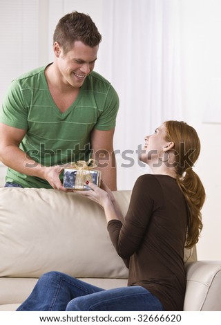 A young man giving a gift to a young woman.  They are smiling at one another. Vertically framed shot.