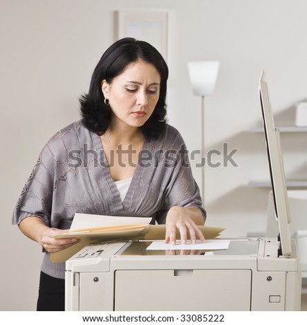 Attractive asian woman making copy on copy machine in office. Looking at paper on machine. Square.