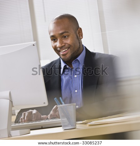 Attractive African American smiling at computer, while sitting at a desk typing on keyboard. Square.