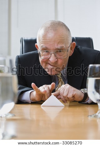 Playful senior male sitting at desk flicking paper football. Vertical