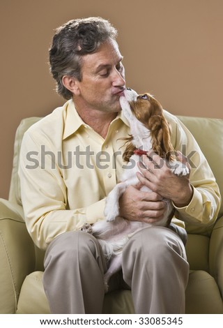 Attractive man sitting on chair, kissing dog on his lap.Looking at dog.Vertical