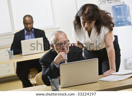 A group of business people are in an office and are working on computers.  They are looking away from the camera.  Horizontally framed shot.