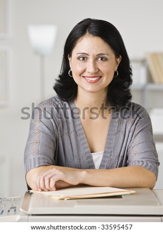 A young businesswoman is standing in an office and smiling at the camera.  Vertically framed shot.