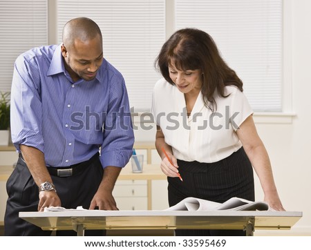 A businessman and woman are working together in an office.  They are looking away from the camera.  Horizontally framed shot.