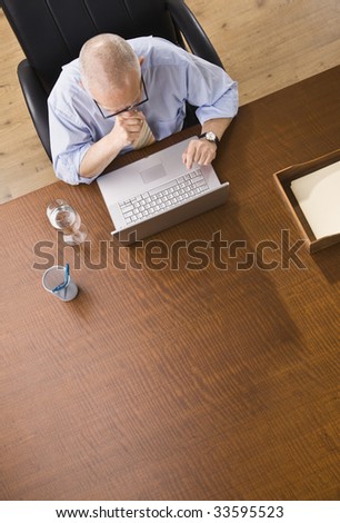 An elderly businessman is working on a laptop in an office.  He is looking away from the camera.  Vertically framed shot.