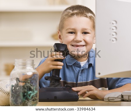 A boy is playing computer games and smiling at the camera.  Horizontally framed shot.