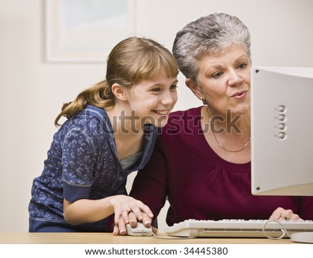 A senior woman and a young girl share a mouse as they use a computer together.