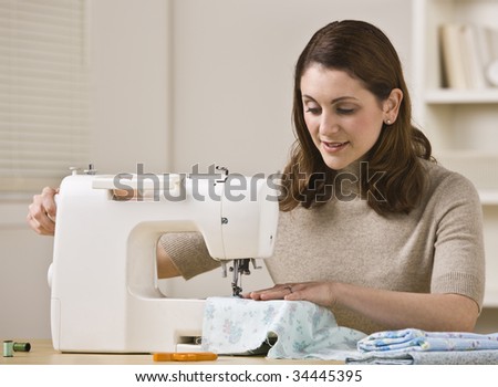 An attractive brunette sewing in her home.  She has a slight smile on her face.  Horizontally framed shot.
