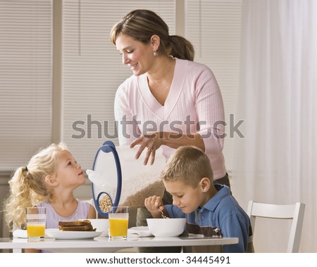 A beautiful family eating breakfast together. The mother is smiling and is pouring cereal for the daughter.  Horizontally framed shot.