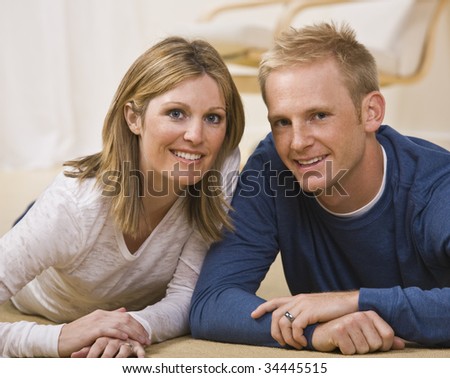 A beautiful couple posing together.  They are lying on the ground and are smiling directly at the camera.  Horizontally framed shot.