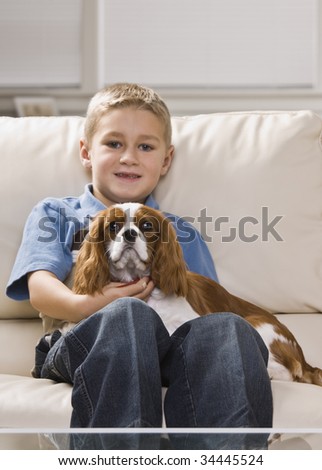 A cute little boy holding a dog on his lap.  He is smiling.  Vertically framed shot.