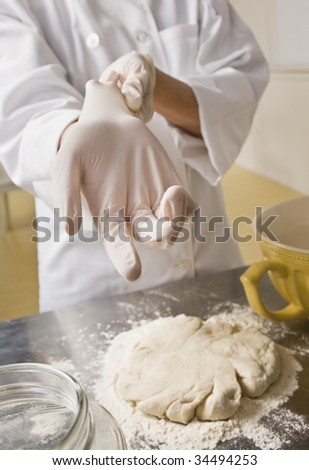 Female chef putting on glove to complete pastry on counter. Vertical.
