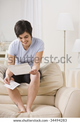 Attractive woman sitting on couch and smiling while reading letter. Vertical