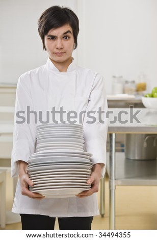 Brunette woman with questioning face, carrying heavy dishes and looking toward camera. Vertical