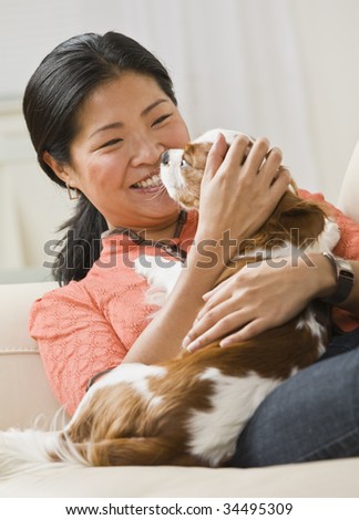 A woman is holding a dog in her arms, smiling, and looking away from the camera.  Vertically framed shot.
