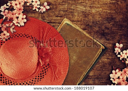 Summer hat, old book and spring blossom on wooden background.
