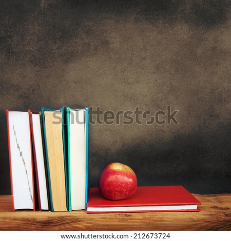 Still life with school books and apple against clean black blackboard on background