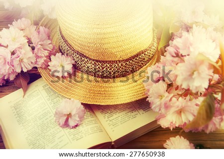 Straw hat, book and spring flowers over wooden table. Relaxation or vacation concept