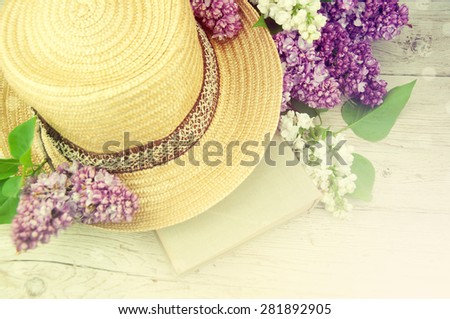 Straw hat, book and lilac flower over wooden table. Relaxation or vacation concept